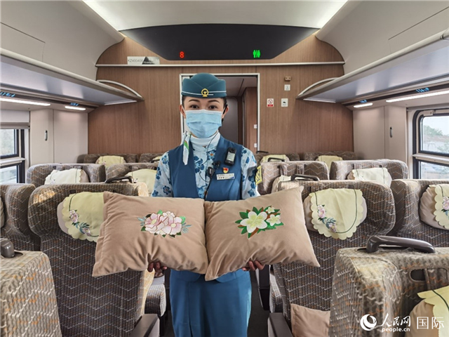 趙瑩靜展示中老鐵路國(guó)際旅客列車?yán)飵в兄袊?guó)牡丹花和老撾占巴花刺繡圖案的靠墊。人民網(wǎng)記者 杜明明攝
